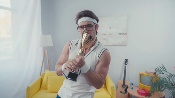 Izgalmas sportoló pózol trófea csésze alatt fénykép villog a nappaliban - Felvétel, videó