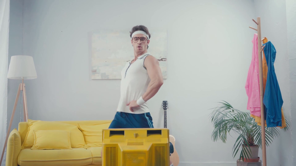 Sportowiec z rękami na biodrach robi skok przed telewizorem retro w domu - Materiał filmowy, wideo