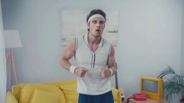 Serious sportsman with headband running in place at home, retro sport conception - Footage, Video