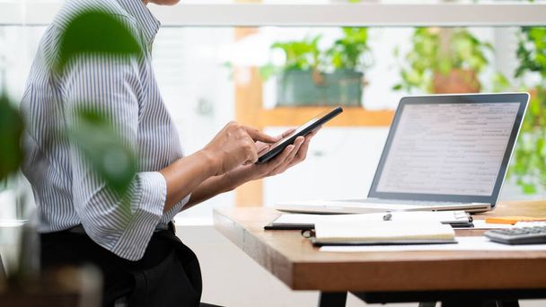 Frauen, die ihr Smartphone in der Hand halten, bekommen die Transaktion auf dem Laptop am modernen Holztisch im Büro - Foto, Bild