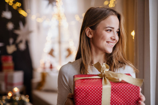 Happy young woman indoors at home at Christmas, holding present. - Valokuva, kuva