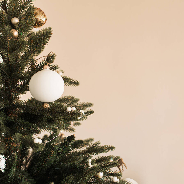 Closeup of Christmas / New Year fir tree decorated with baubles. Holiday celebration composition on beige background. - 写真・画像