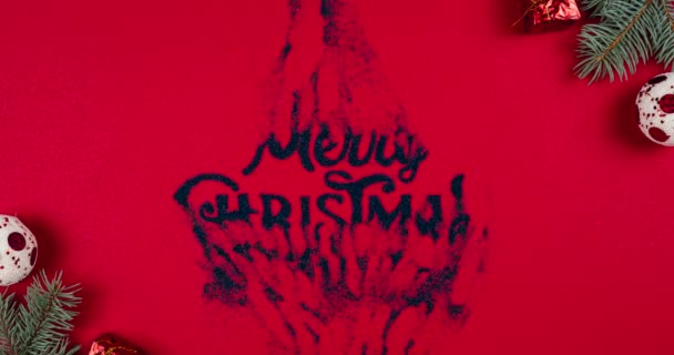 Buon Natale lettering appare su sfondo rosso, rami di abete e palle di Capodanno intorno. Animazione stop motion, posa piatta. Concetti di biglietto di auguri. Vista dall'alto. - Filmati, video