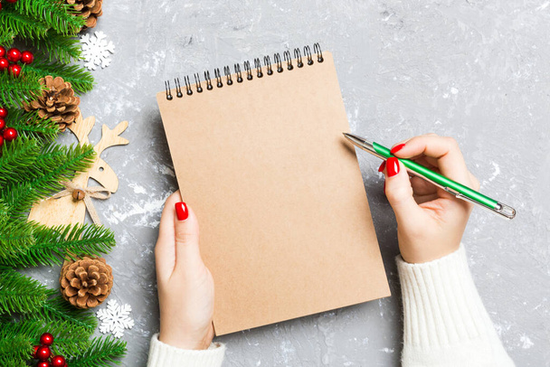 Top view of female hand writing in a notebook on cement Christmas background. fir tree and festive decorations. Wish list. New Year concept. - Photo, Image