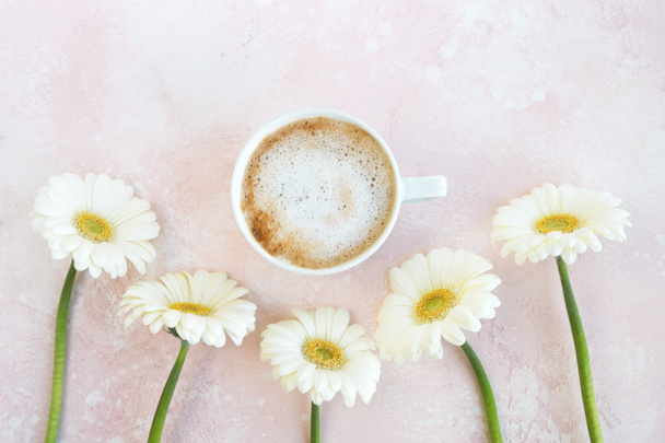 Šálek kávy s gerbera sedmikrásky květiny na pastelovém pozadí. Ranní snídaně, pozdrav. Minimální složení. Pohled shora, byt ležel - Fotografie, Obrázek