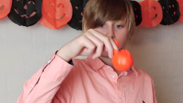 Ένα ξανθό αγόρι να διασκεδάζει κουνώντας το πορτοκαλί μπαλόνι κολοκύθας με το πρόσωπο του Jack 'O Lantern, φουσκωμένο μπαλόνι, αποκριές στο σπίτι με διακοσμήσεις - Πλάνα, βίντεο
