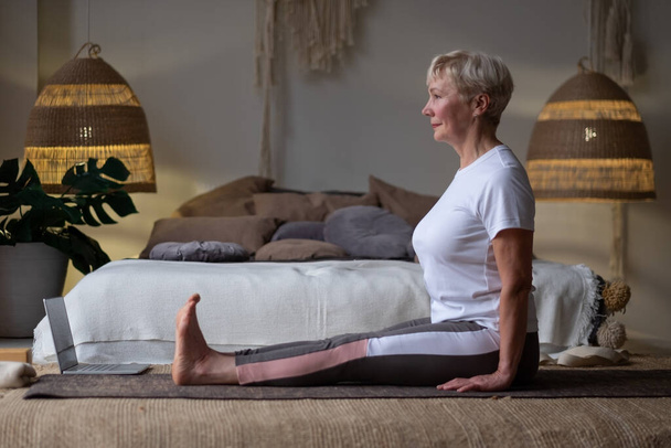 Mujer mayor practicando yoga, sentada en casa en el ejercicio de Dandasana - Foto, Imagen
