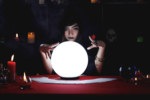 Fortune teller σε μαύρο κουκούλα πρόβλεψη μελλοντική εκδήλωση ή πεπρωμένο με τη χρήση κρυστάλλινη σφαίρα. - Φωτογραφία, εικόνα