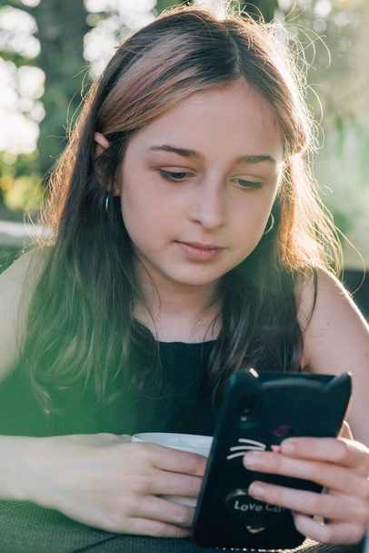 Menina adolescente usando seu telefone celular, enquanto toma uma xícara de chá shalllow DOF, cor tonificada imagem. Adolescente bebe chá e olha para um smartphone. - Foto, Imagem