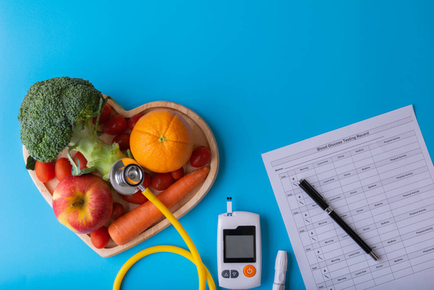 World diabetes day. National American diabetic awareness. Free Glucose Monitors on blue background. Yellow stethoscope check fruit on heart plate. Healthcare and medical concept - Fotoğraf, Görsel