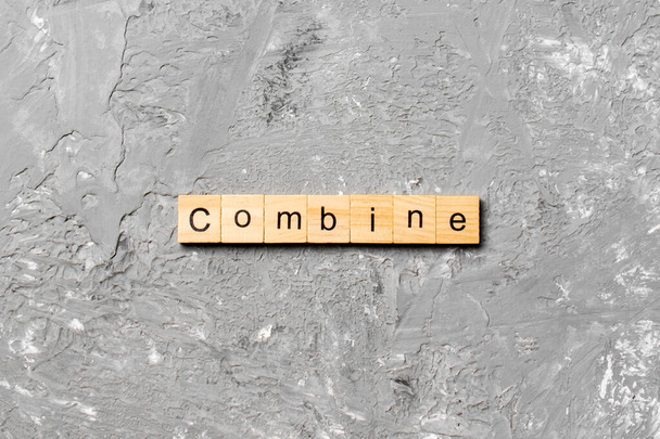 KOMBINE słowo napisane na bloku drewna. COMBINE tekst na cementowym stole do projektowania, koncepcja. - Zdjęcie, obraz