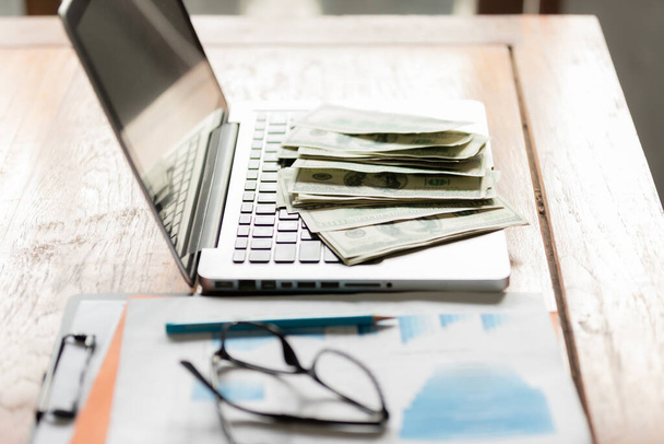 Büroarbeitsplatz mit Laptop und Bargeld auf Holztisch. Konzept von Reich mit Geschäft. - Foto, Bild