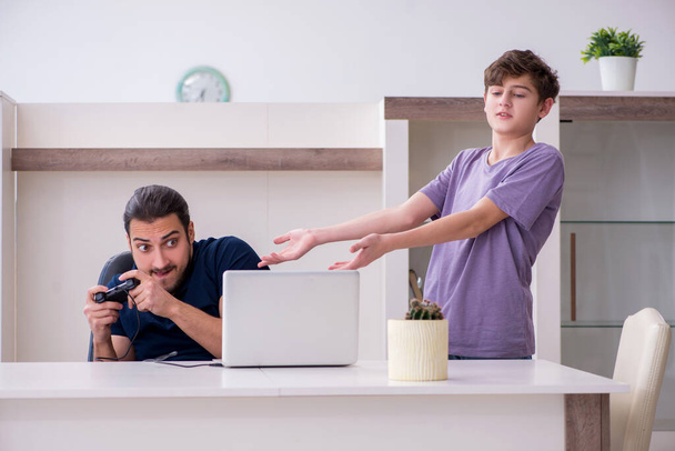 Νεαρός πατέρας και μαθητής παίζουν παιχνίδια στον υπολογιστή στο σπίτι - Φωτογραφία, εικόνα