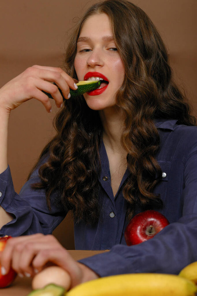 Young woman in group of fruit. Healthcare and healthy nutrition concept. bites an avocado - Φωτογραφία, εικόνα