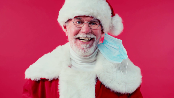 Joulupukki riisuu lääketieteellisen naamion ja hymyilee kameralle eristettynä punaiseen - Materiaali, video
