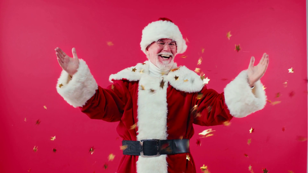 opgewonden santa claus onder glinsterende ster-vormige confetti geïsoleerd op rood - Video