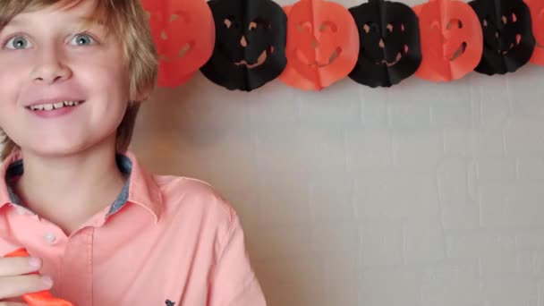 Blonďatý chlapec se usmívá Nafukovací oranžový dýňový balón s obličejem Jacka O Lanterna, slaví Halloween doma slavnostní výzdobou - Záběry, video