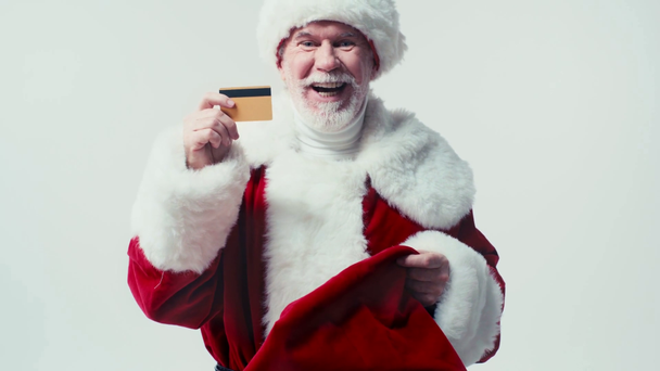 cheerful santa claus getting credit card out of sack isolated on white - Materiał filmowy, wideo