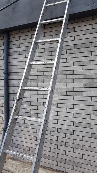 Stalen dwarsbalken van de constructie ladder in de voorkant van grijze bakstenen muur van modern gebouw. Reparatieapparatuur - Foto, afbeelding