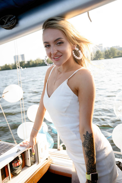 Beautiful young sexy blond woman in a dress and makeup, summer trip on a yacht with white sails on the sea or ocean in the Gulf marine of the wind and the breeze in the sun tans romantic - Zdjęcie, obraz