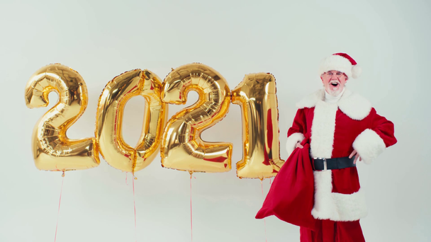 διεγερμένος Άγιος Βασίλης με σάκο κοντά σε μπαλόνια σε σχήμα 2021 απομονωμένος σε λευκό - Πλάνα, βίντεο