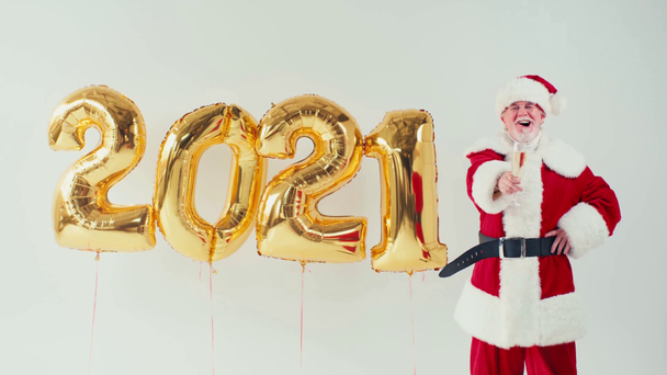 Weihnachtsmann mit Champagner in der Nähe von Luftballons in Form von 2021 isoliert auf weiß - Filmmaterial, Video
