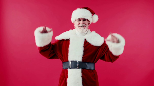 onnellinen joulupukki seisoo kädet lantiolla ja avoimet kädet eristetty punaisella - Materiaali, video