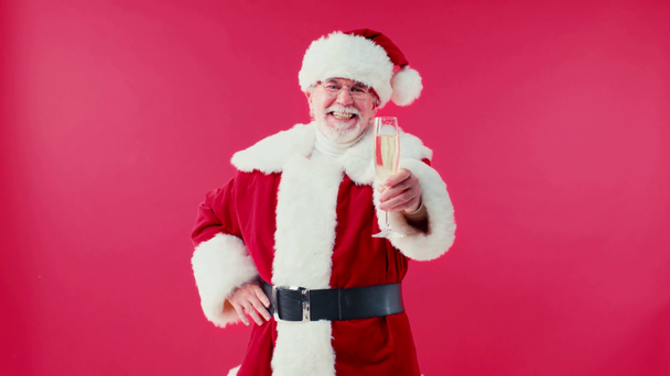 vrolijk santa claus met de hand op heup vasthouden champagne glas geïsoleerd op rood - Video