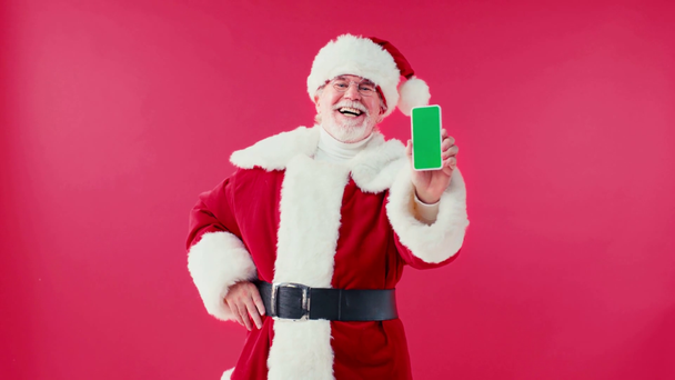 happy santa claus showing smartphone with green screen isolated on red - Footage, Video