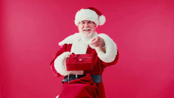 Santa Claus dostává dárkovou krabici z pytle, ukazuje prstem izolovaným na červenou - Záběry, video