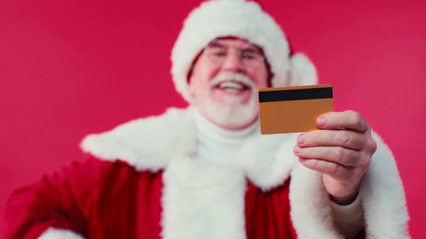 Papai Noel apontando para o cartão de crédito em fundo borrado isolado em vermelho - Filmagem, Vídeo