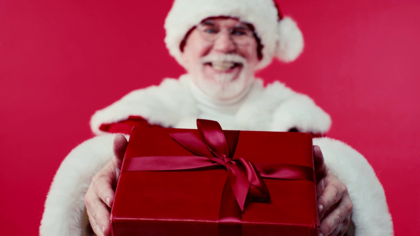 alegre santa claus hablando y presentando caja de regalo aislado en rojo - Imágenes, Vídeo