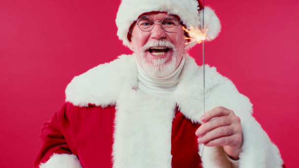 joyful santa claus talking and holding sparkler isolated on red - Footage, Video