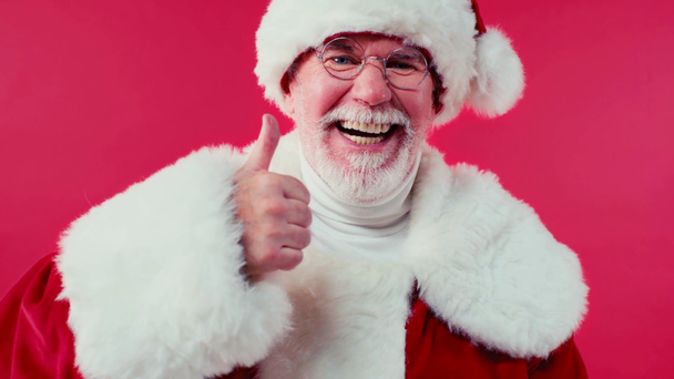 cheerful santa claus showing thumb up isolated on red - Кадри, відео