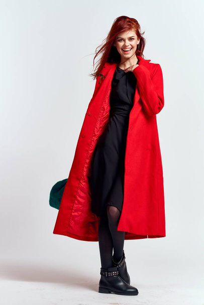 Kırmızı ceketli, şapkalı, açık renk arka planda siyah çizmeli, duygusal bir kadın model. - Fotoğraf, Görsel