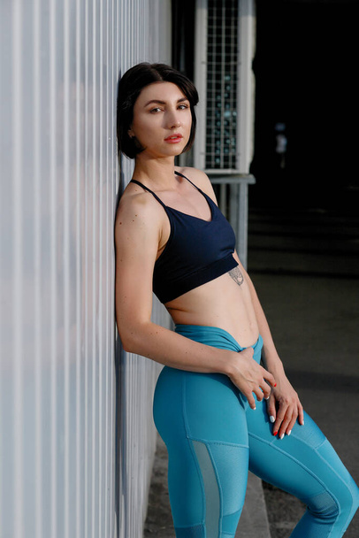 Tough young woman in sports wear staring at camera. Sportswoman taking a breather after training outdoors. - Foto, Imagen