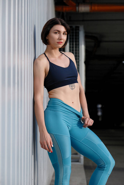 Tough young woman in sports wear staring at camera. Sportswoman taking a breather after training outdoors. - Foto, afbeelding