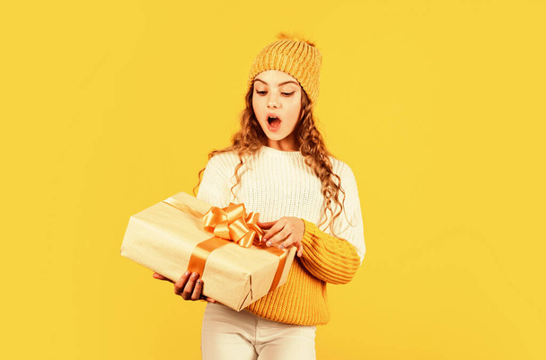 Child excited unpacking gift. Christmas present for daughter. Enjoy surprises. Kid little girl hold gift box with ribbon on yellow background. Teen girl received holiday gift. Best christmas gifts - Fotoğraf, Görsel