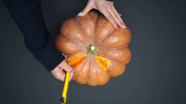 partial view of woman holding knife and carving creepy pumpkin on black - Footage, Video