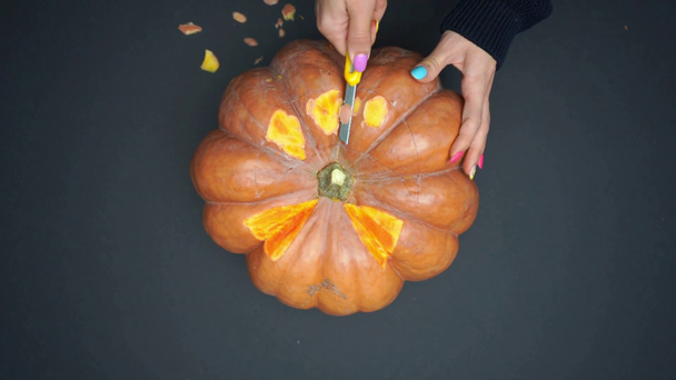 top view of woman holding knife and carving creepy pumpkin on black - Footage, Video