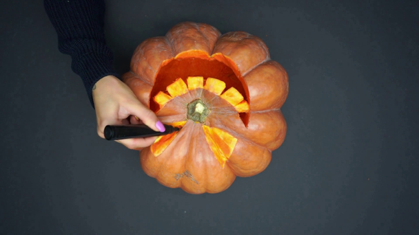 top view of woman holding marker pen near carved and creepy pumpkin on black - Materiaali, video