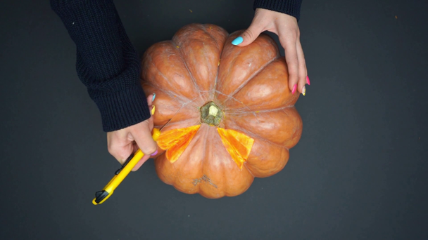 top view of woman carving ripe pumpkin with knife on black - Footage, Video