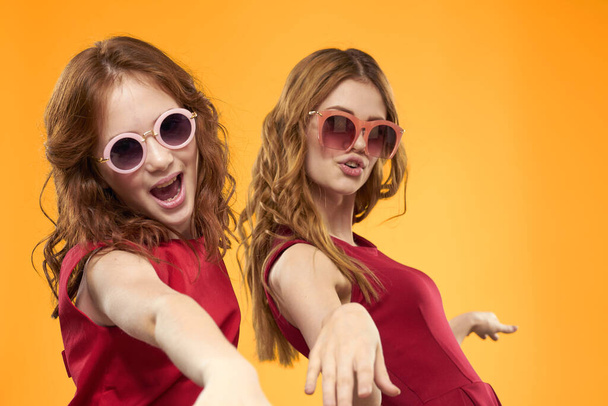 Happy sisters in red dresses on a yellow background are having fun and gesticulating Copy Space - Foto, Imagen