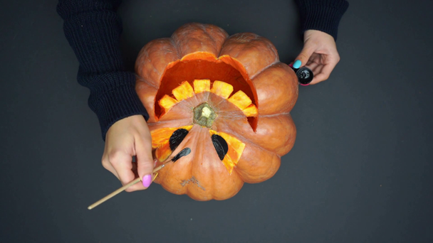 top view of woman with paintbrush in hand painting on carved pumpkin on black - Footage, Video