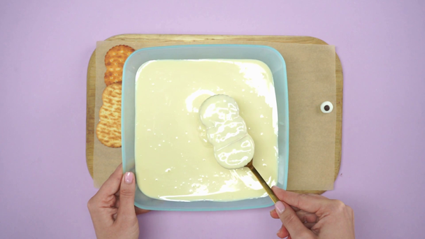 bovenaanzicht van vrouw het nemen van koekje in crème met vork op licht paars - Video