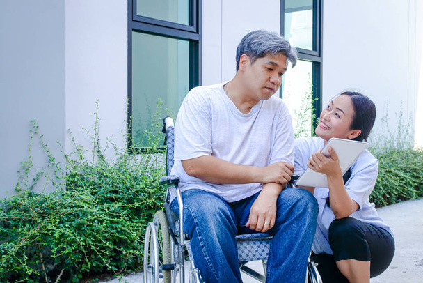 Το κορίτσι φροντίζει τον άντρα ασθενή που κάθεται στην αναπηρική καρέκλα. Θέλει να επιστρέψει δυνατός και πάλι.. - Φωτογραφία, εικόνα