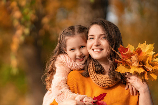 Happy family! Mother and daughter hugging and playing and laughing at the autumn stroll. The girl hugs her mother holding a bouquet of colorful autumn maple leaves. They have a great time together. - Foto, immagini