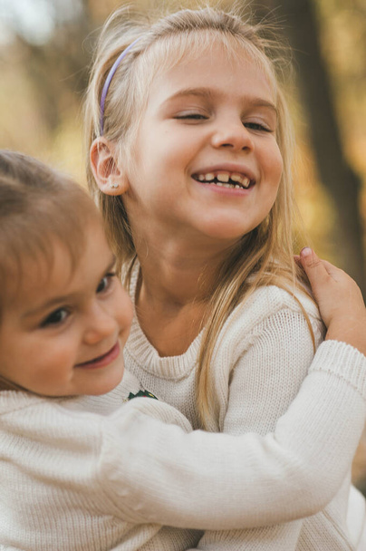 Zwei fröhliche kleine Schwestern, die an warmen Herbsttagen im Park spielen. Familienkonzept, Liebeskonzept, herbstlicher Hintergrund - Foto, Bild