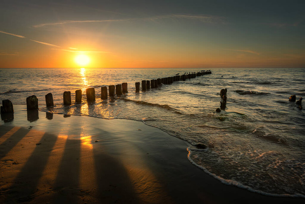 Ostseestrand bei Sonnenuntergang. Wellenbrecher aus Holz. Aufbruch in Polen - Foto, Bild