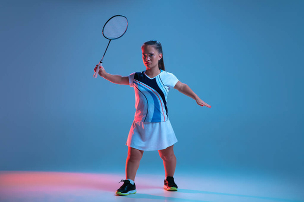 Beautiful dwarf woman practicing in badminton isolated on blue background in neon light - 写真・画像